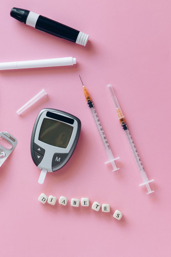 about-us-02 Close-up of diabetes monitoring tools with syringes and blocks spelling 'diabetes' on a pink background.